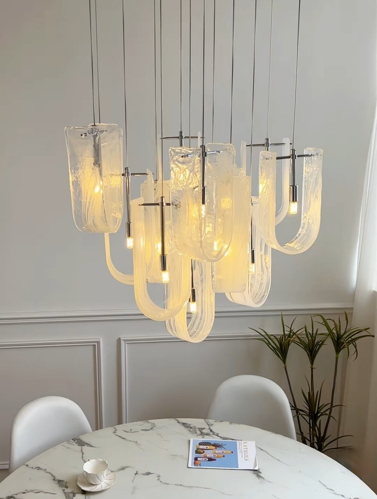 Luminous Waves Chandelier by Aurorae Lighting gracefully illuminating a modern dining room table, creating a warm, inviting ambiance.