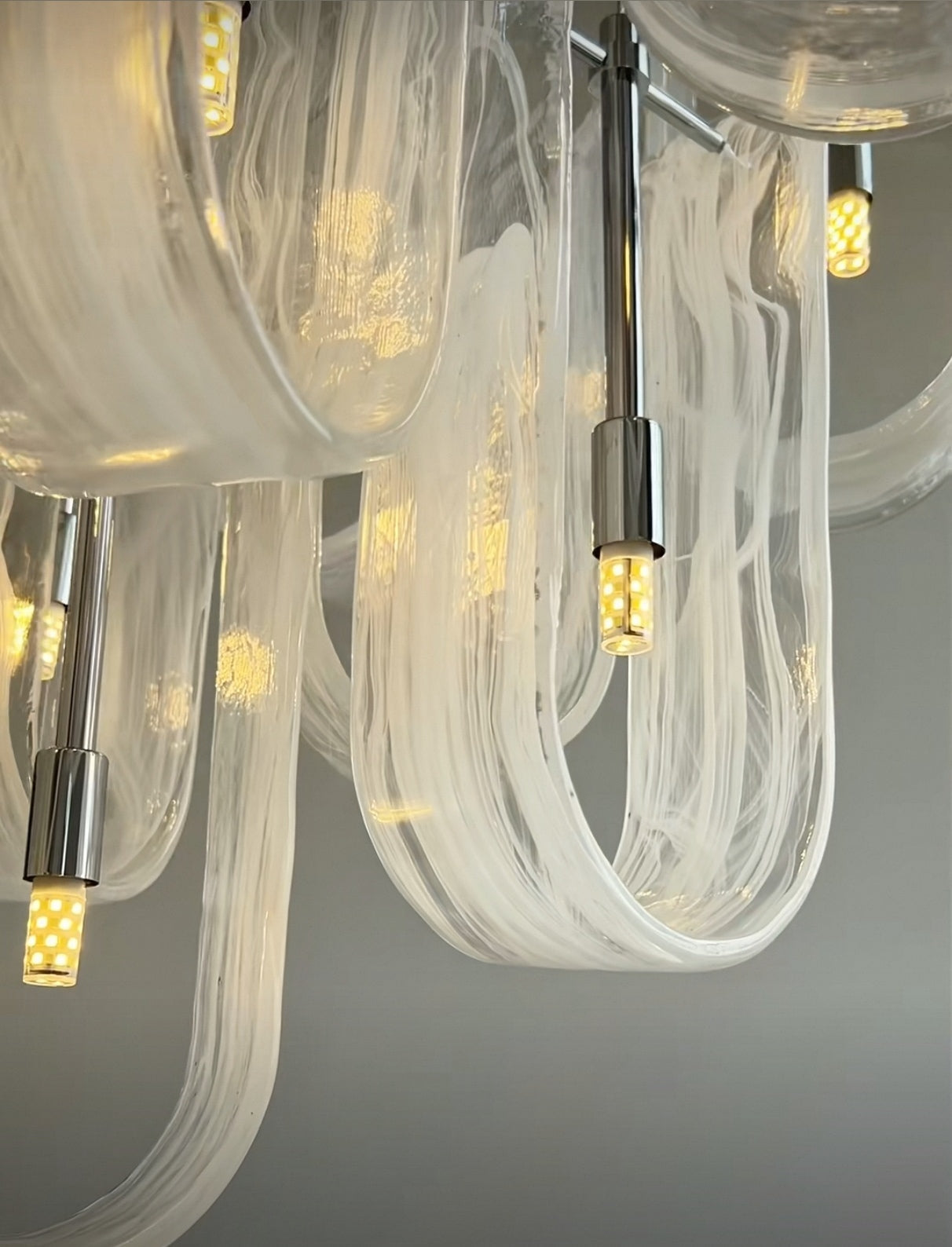 Illuminated detail of a single wave segment from Aurorae Lighting's Luminous Waves Chandelier, revealing its smooth texture and radiant light.