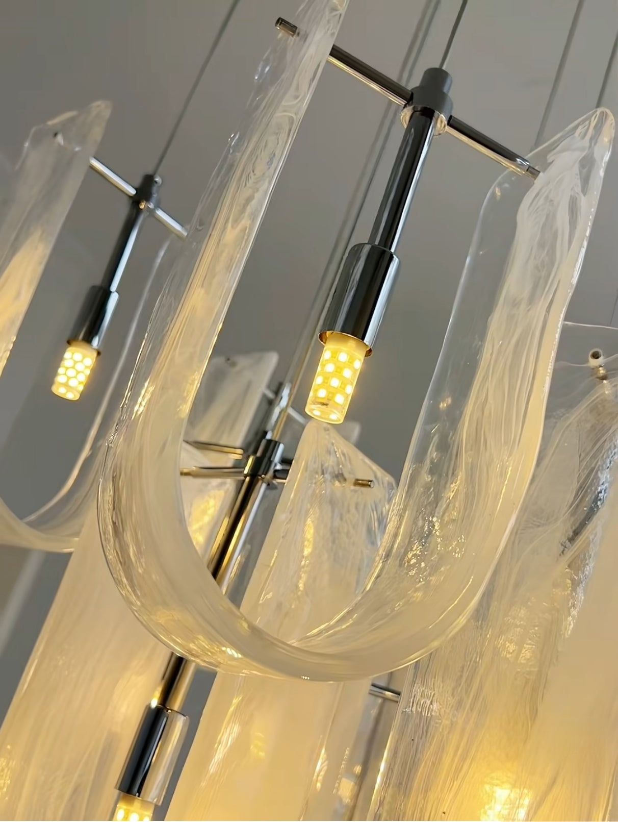 Detailed close-up of the Luminous Waves Chandelier's polished gold finish and the bright, even light emanating from its curved LED elements.