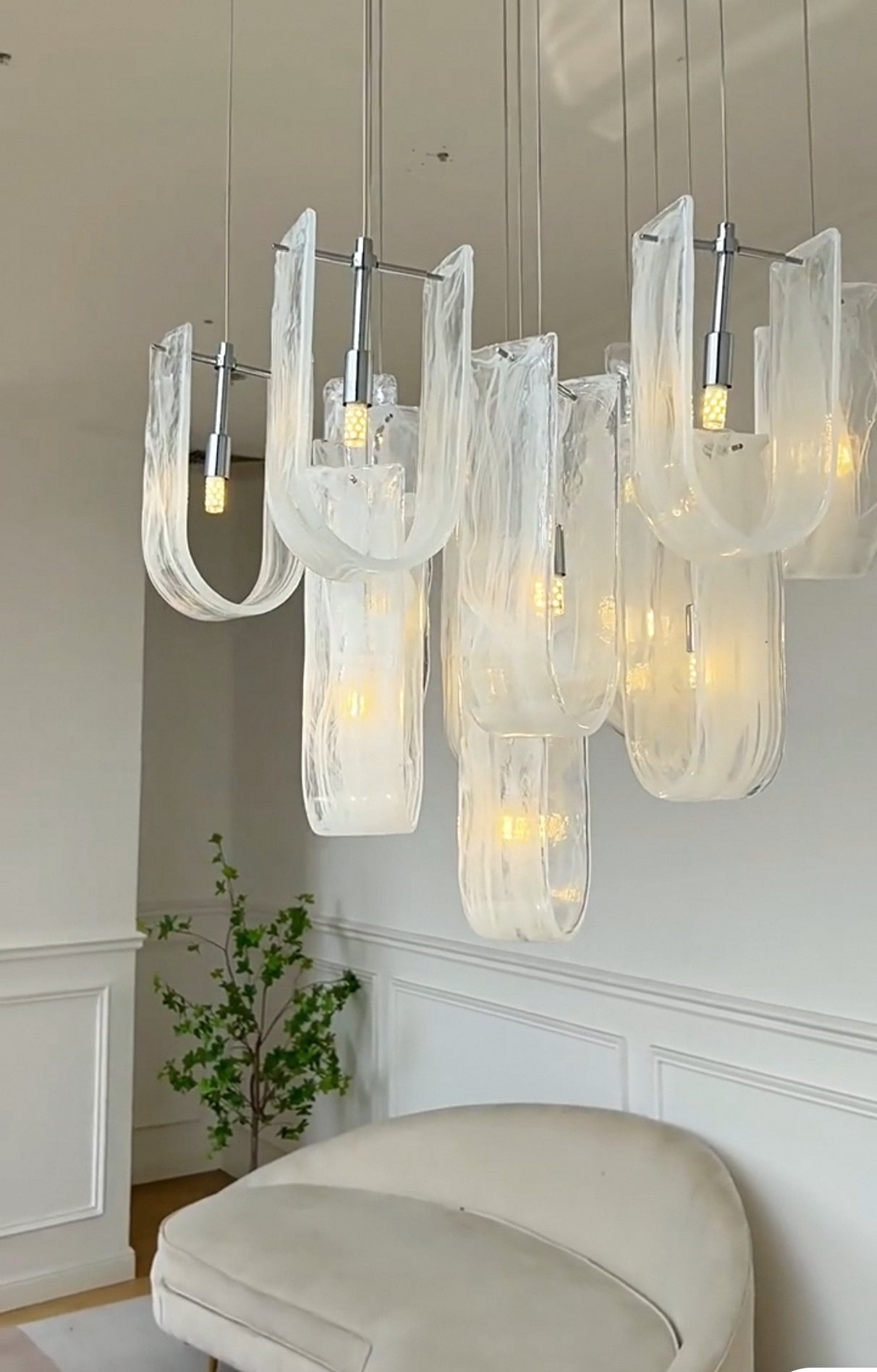 The Luminous Waves Chandelier casting an ambient glow in a stylish bedroom, adding a touch of modern elegance above the seating area.