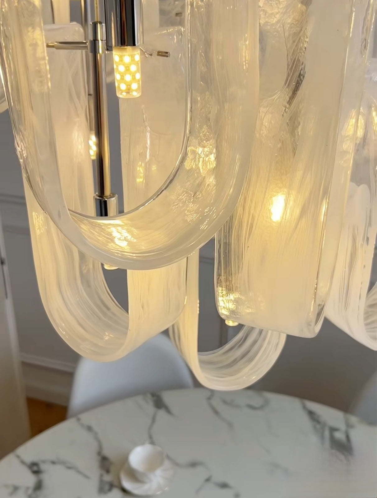 The Luminous Waves chandelier installed above a modern dining table, creating an inviting atmosphere.