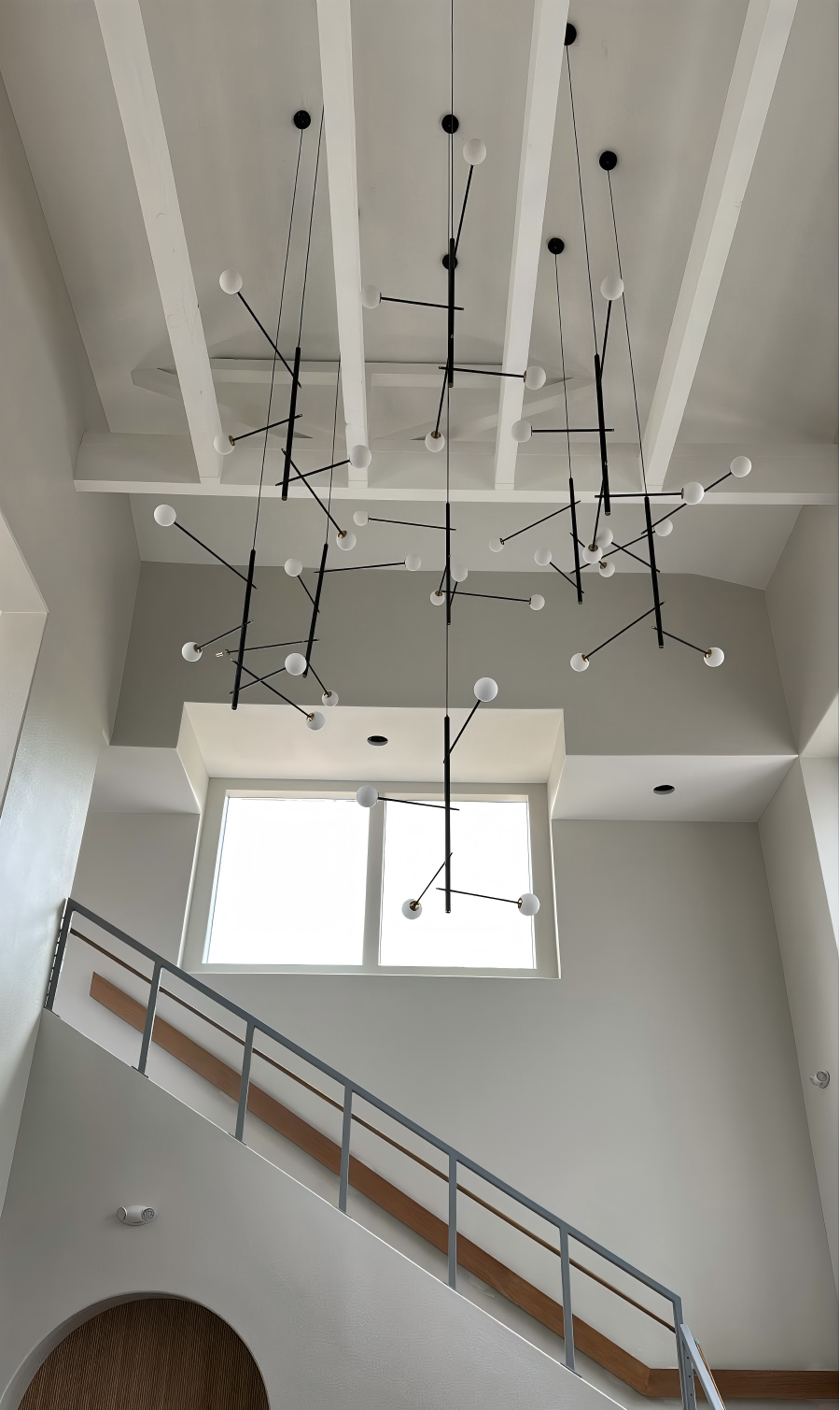 Black multi-arm opal glass chandelier hanging in a spacious modern entrance, next to stairs.