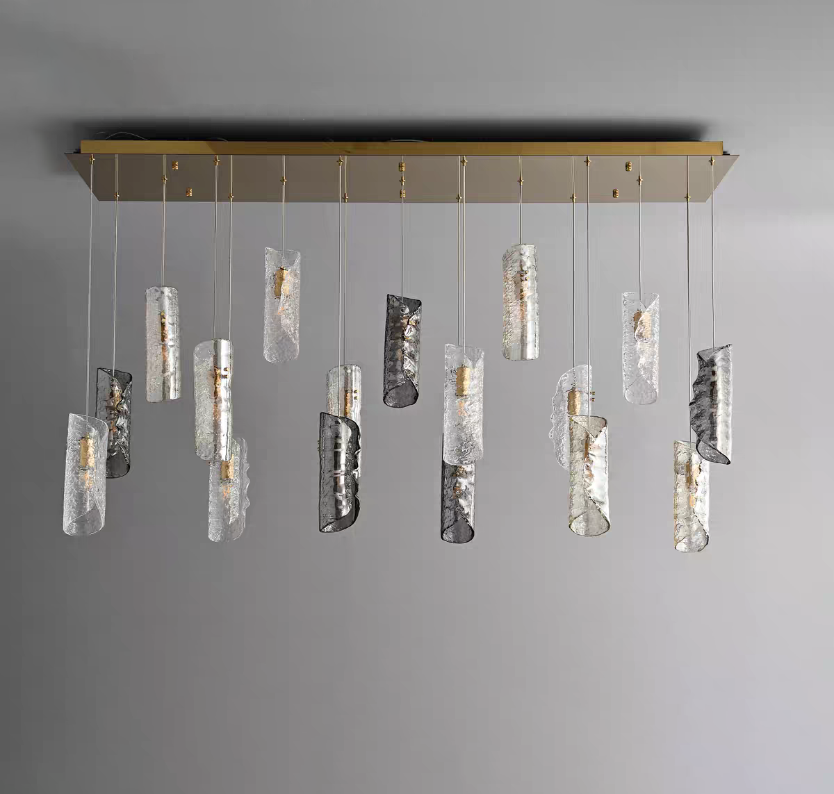 Expansive Aurorae Lighting 17-light multi-pendant chandelier showcasing a linear cascade of artisan textured glass tube shades in clear and smoky grey, all suspended from a sleek brass rectangular canopy.