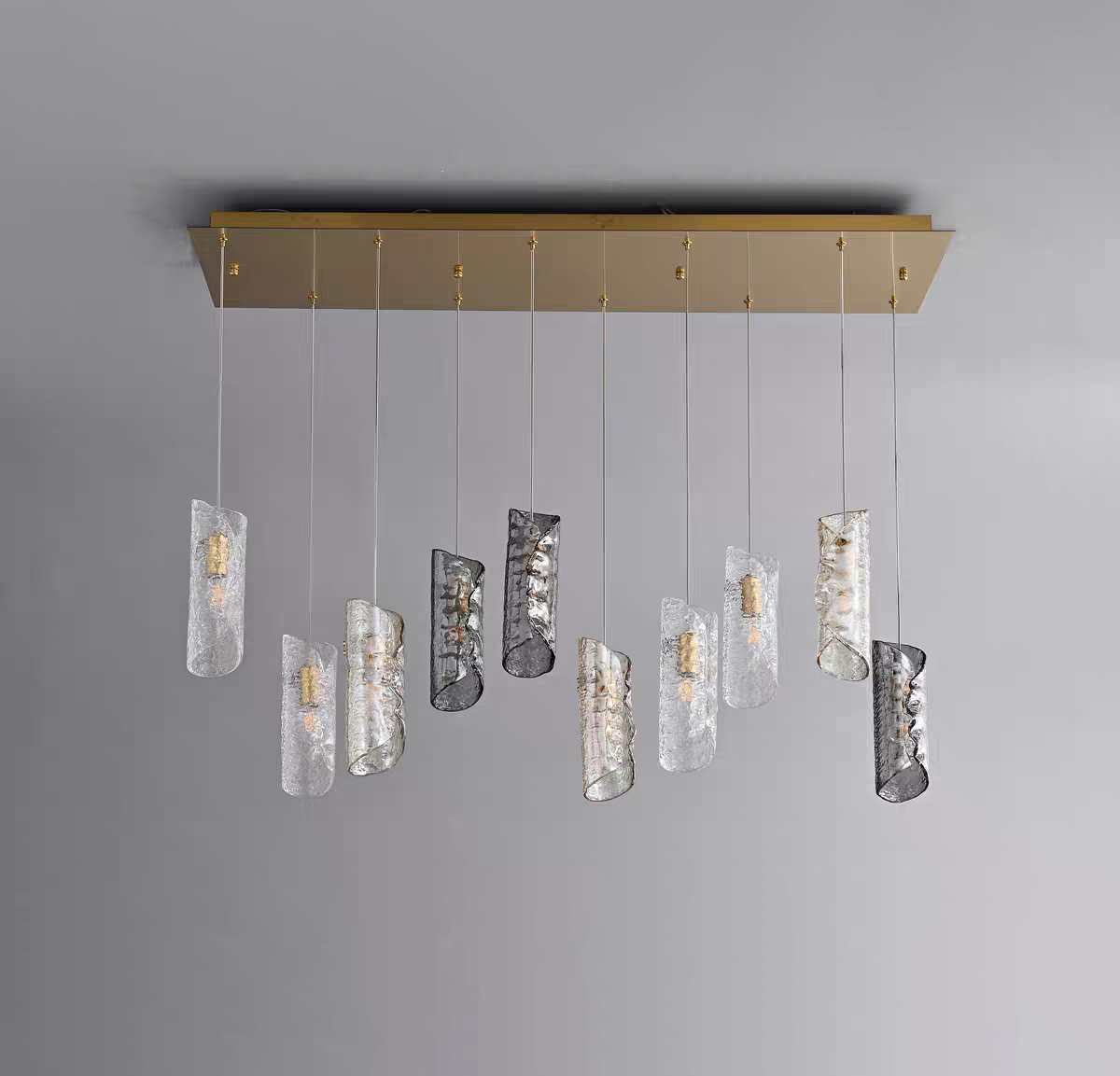 Aurorae Lighting 10-light multi-pendant chandelier featuring staggered artisan textured glass tube shades in clear and smoky grey, suspended from a brass rectangular canopy.
