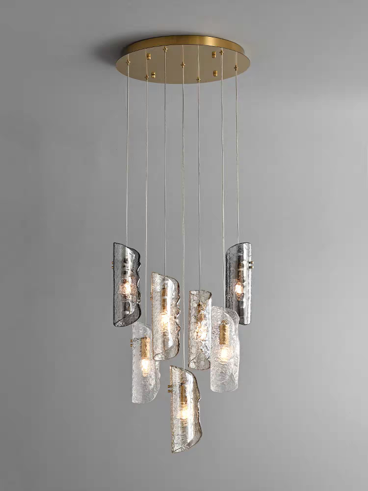 An Aurorae Lighting 7-pendant chandelier gracefully displays its staggered, textured glass tube shades—a blend of clear and smoky grey—suspended from a distinct, round brass-finish canopy.