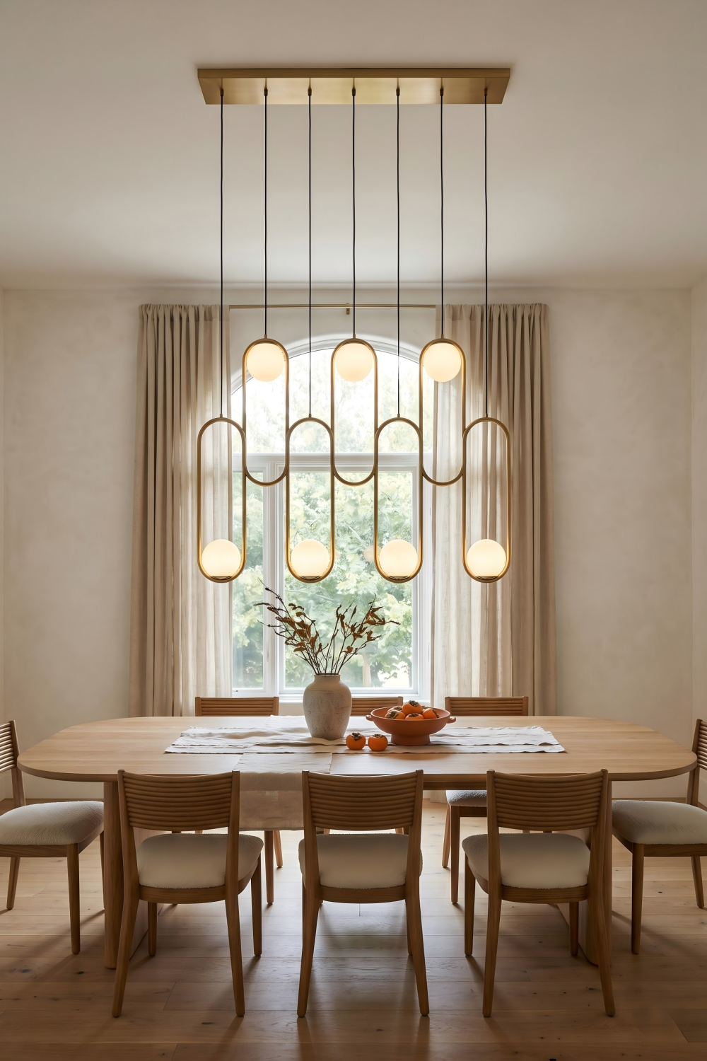 modern opal glass globe chandelier above an oval oak dining table in a minimalist dining room with a large arched window