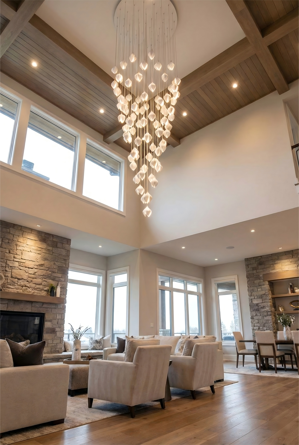 Modern living room with a large chandelier, comfortable furniture, and large windows.